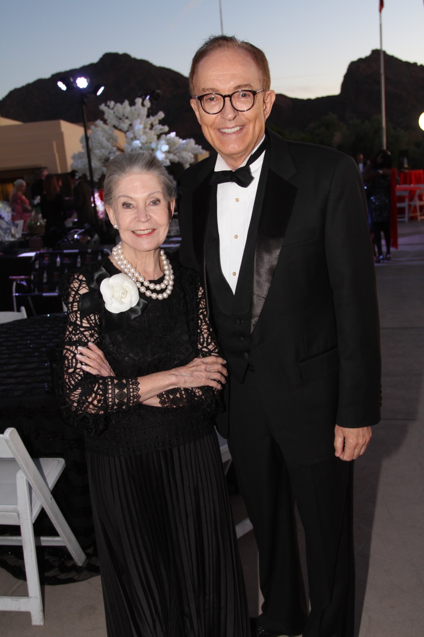 Two guests in black evening attire at an outdoor reception.