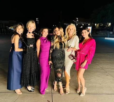 Six guests in evening dresses standing together beside a pool.