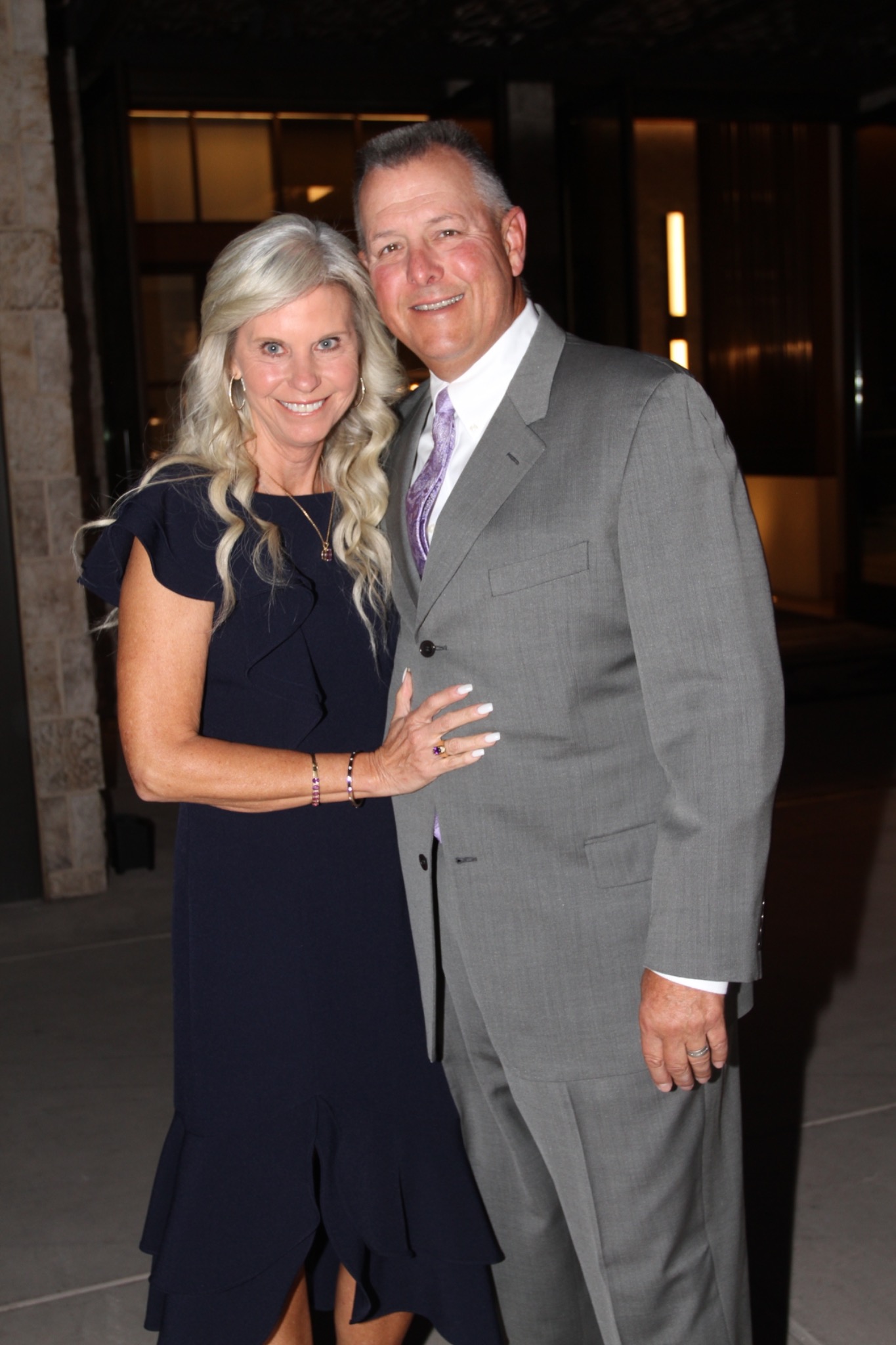 Two guests in navy and gray attire posing at an evening gathering.