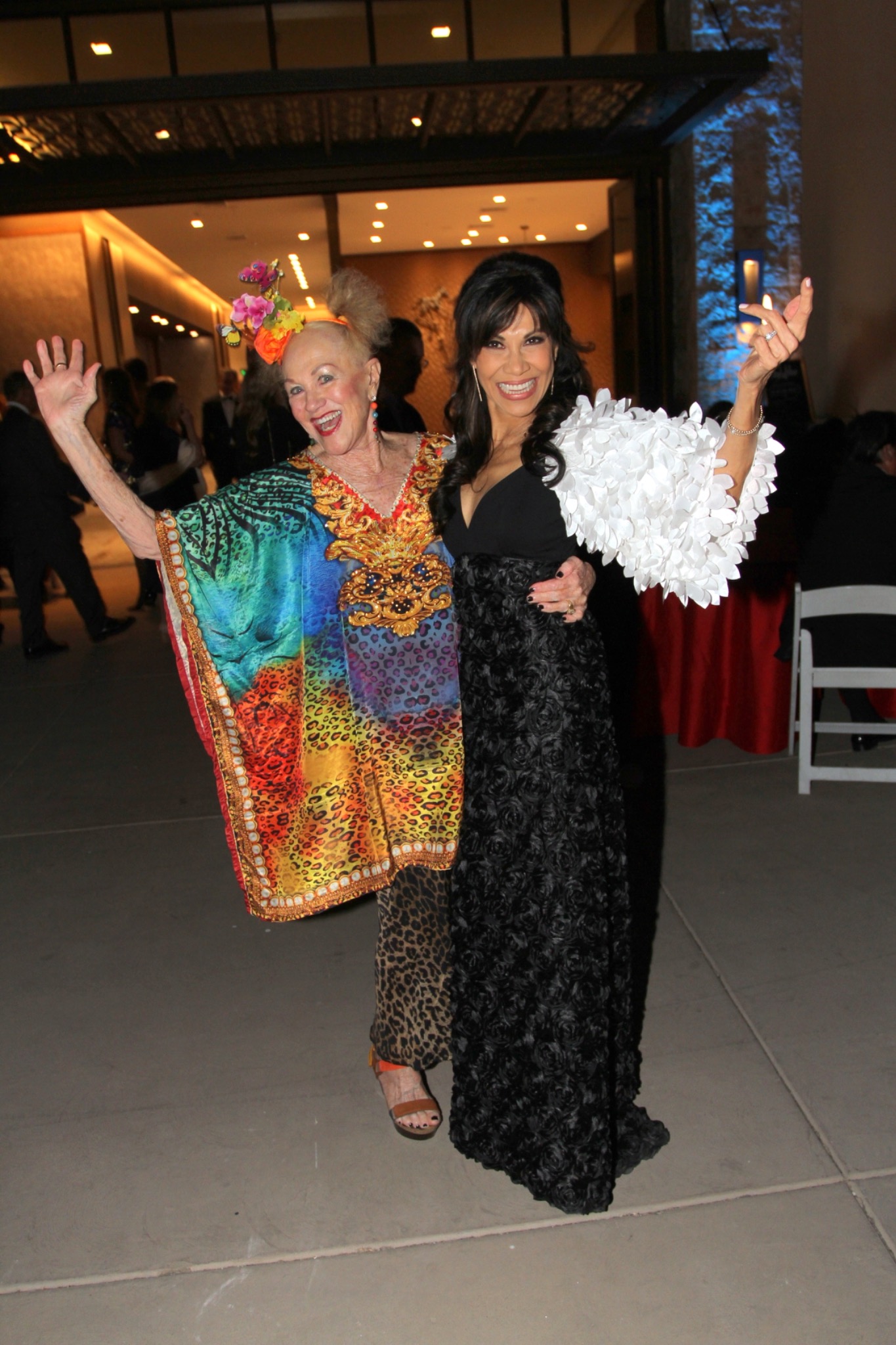 Two guests in colorful and black evening attire celebrating with raised hands.