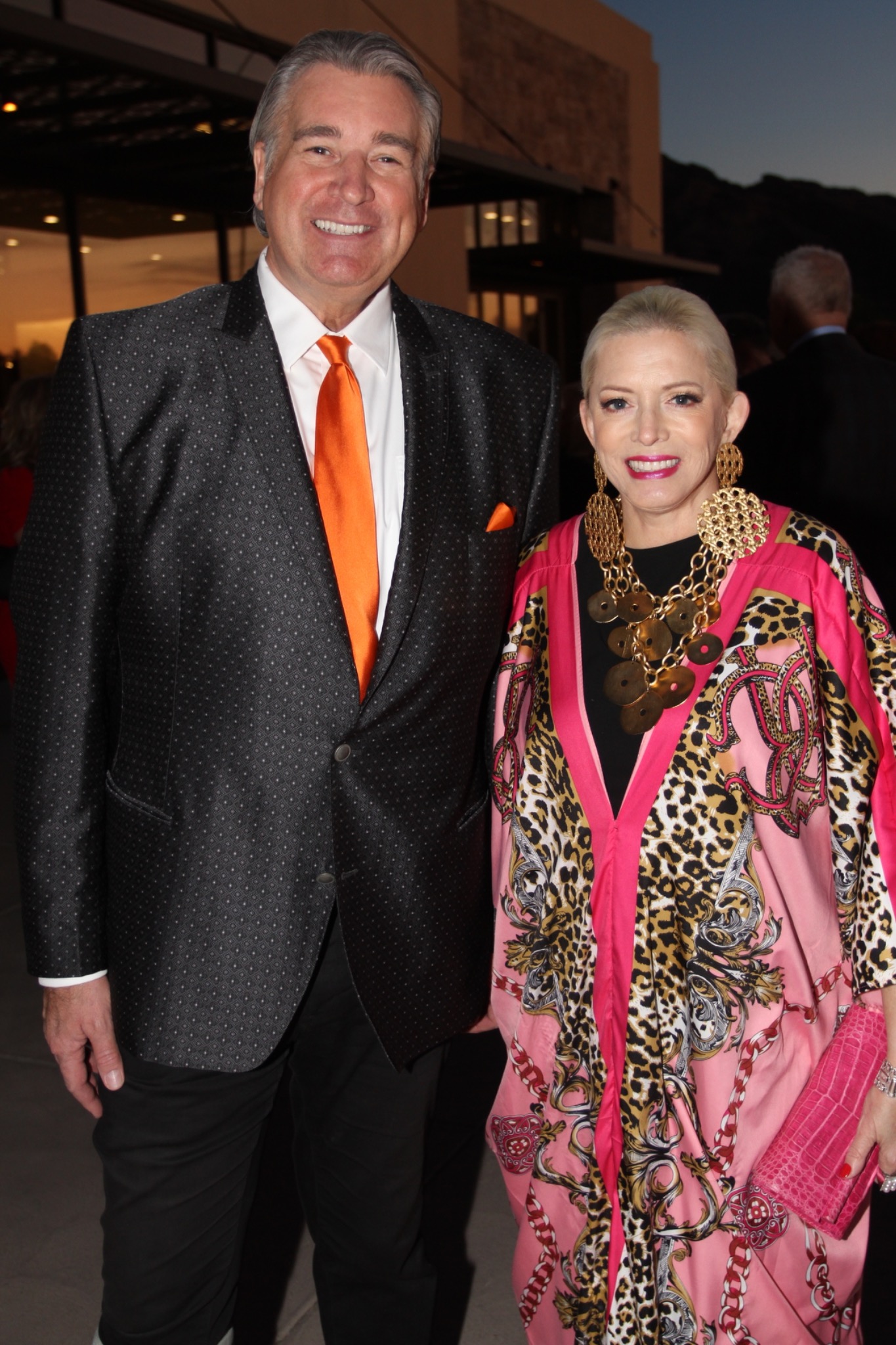 Two guests in a dark suit with an orange tie and a colorful patterned outfit.