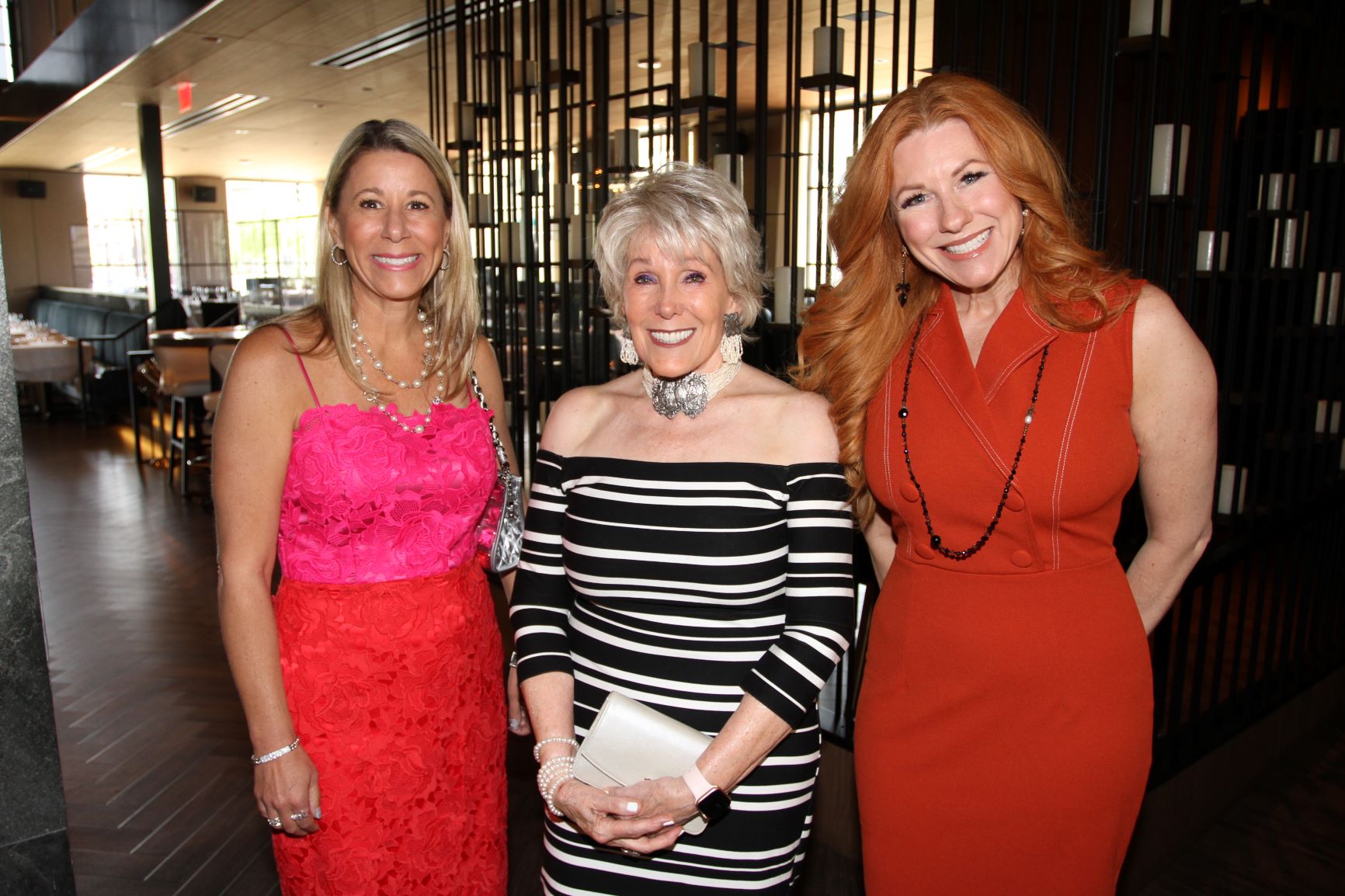 Three guests in pink, striped, and rust-colored dresses at a daytime reception.
